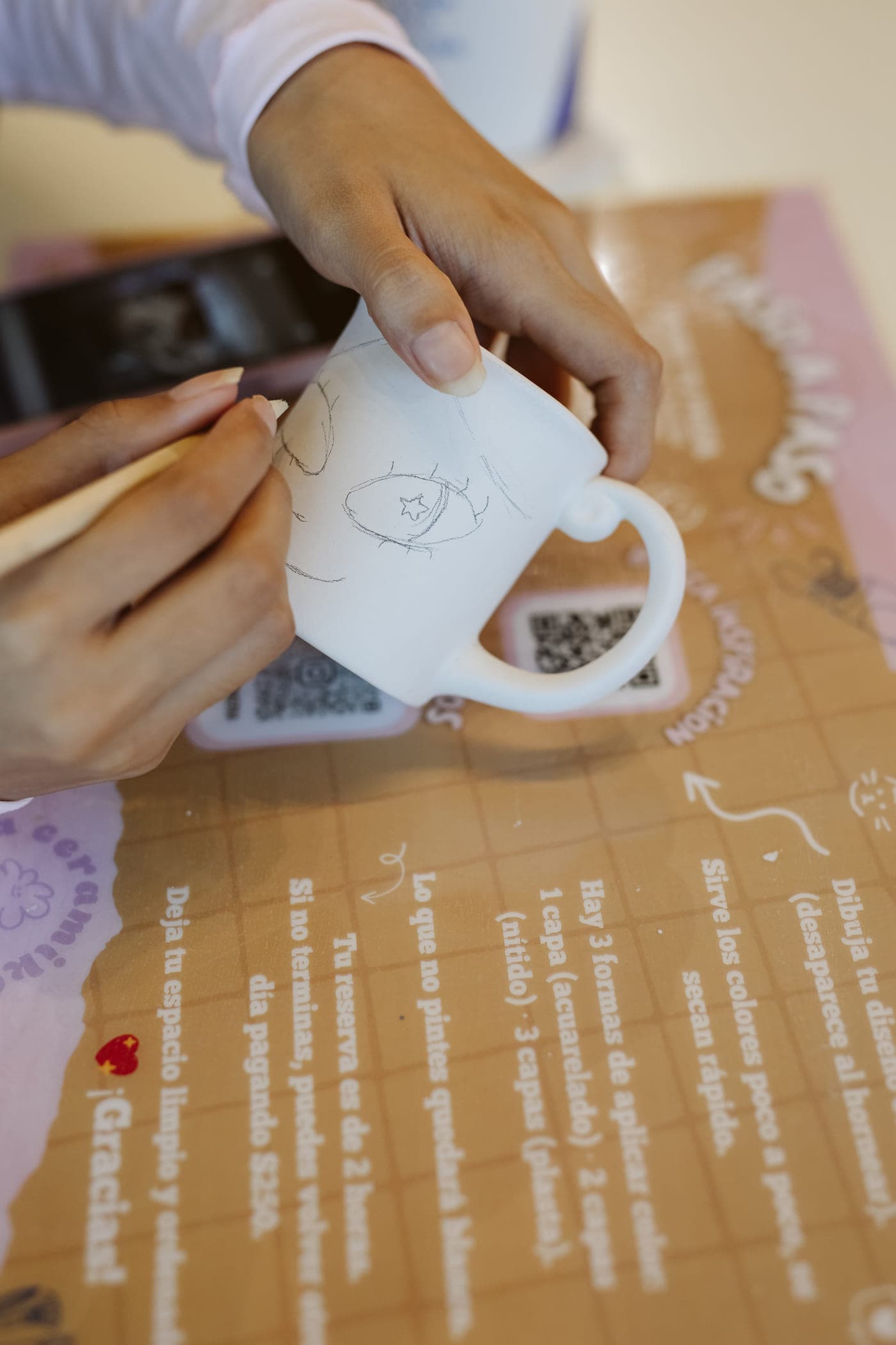 Persona dibujando su diseño a lápiz sobre una taza antes de pintarla