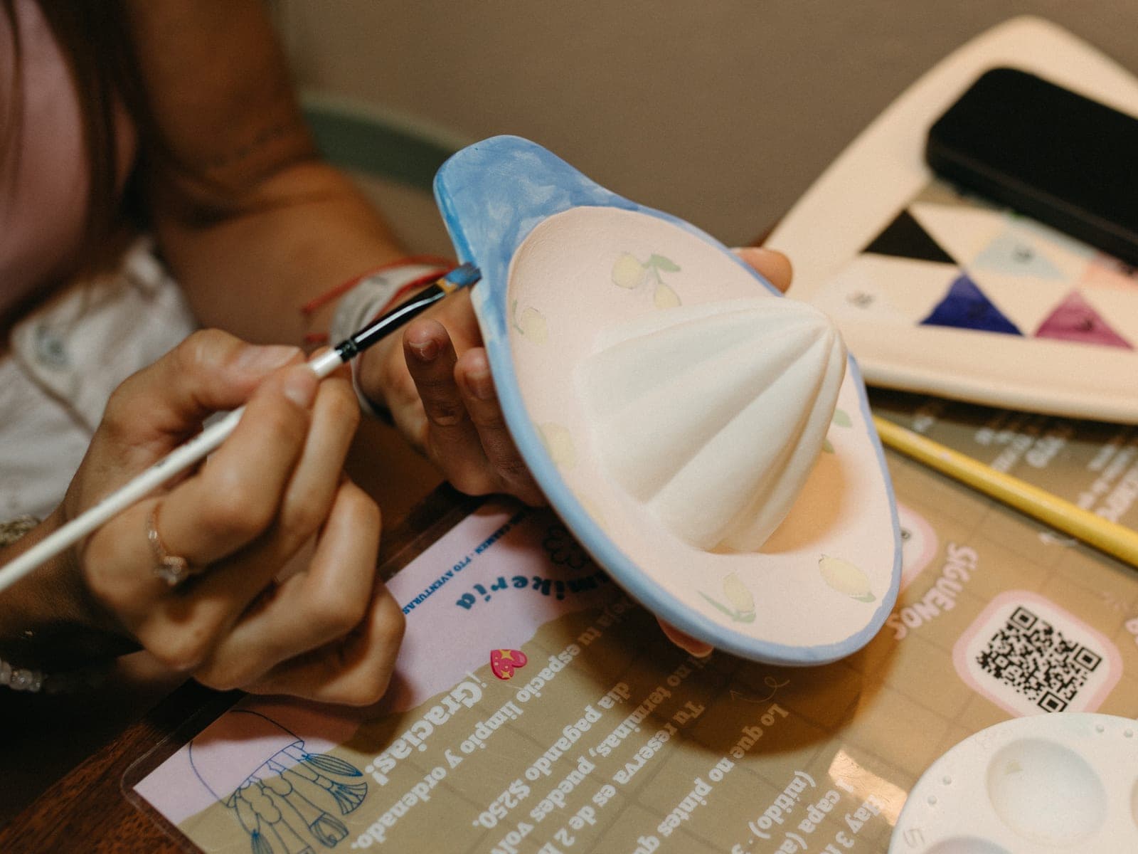 Manos pintando con pincel un exprimidor de cerámica con diseño de limones y borde azul